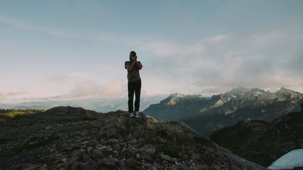 Man takes a picture standing on top of mountain at dusk