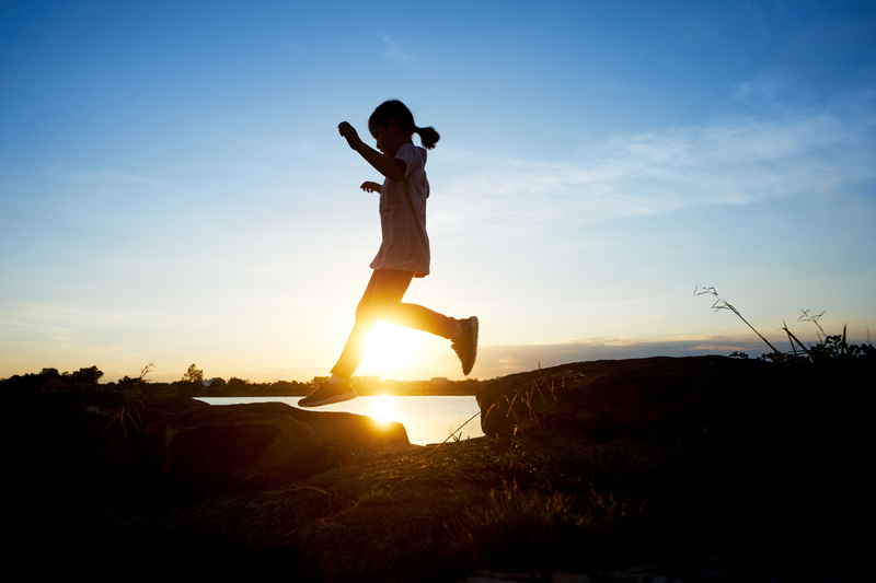 The silhouette of a girl jumping over a stone gap